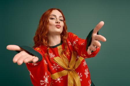 Young woman with red hair poses playfully in a Christmas sweater, ready for holiday fun.の写真素材