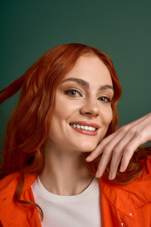 A young woman with flowing red hair smiles brightly in an orange shirt, embodying autumn style.の写真素材