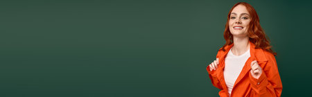 The young redhead smiles brightly, showcasing her orange shirt amidst a green background, bannerの写真素材