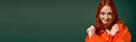 A young redhead woman poses in an orange shirt, radiating joy in an autumn setting, bannerの写真素材
