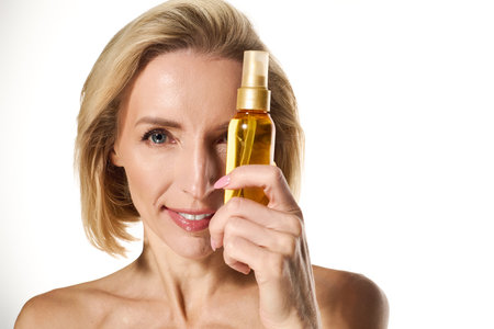 A beautiful woman holds a skin care product while smiling, promoting healthy skin and wellness.の写真素材