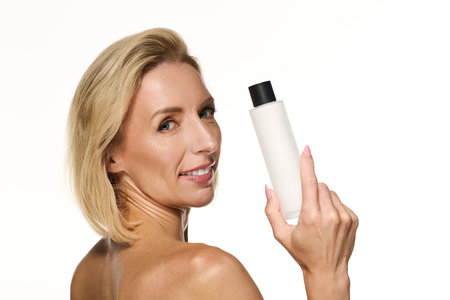 A confident blonde woman with short hair showcases her favorite skincare product, promoting beauty.の写真素材
