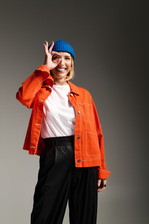 A fashionable blonde woman smiles playfully while wearing an orange jacket and blue beanie.の写真素材
