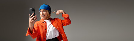 A stylish blonde woman smiles and poses with her phone in a trendy outfit at a studio, bannerの写真素材