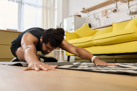 Athletic man with a beard and curly hair stretches on the floor in a cozy home setting.