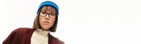 Fashionable young woman with a stylish hat and glasses stands confidently against a light backdrop.