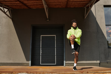 An athletic man with a beard stretches outdoors in a bright green hoodie, focusing on fitness.