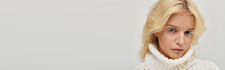 A young blonde woman with unique white eyelashes poses in a cozy knitted sweater, bannerの写真素材