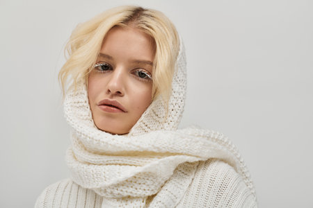 Young blonde woman showcases beauty in a cozy knitted sweater, radiating warmth and style.の写真素材