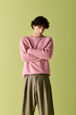 Handsome man poses gracefully, showcasing trendy attire in a chic indoor setting with a green wall.の写真素材