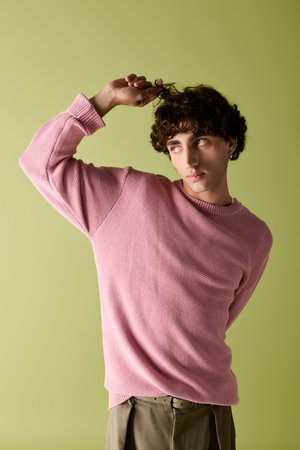 Handsome man in fashion forward outfit playfully styles his hair with a charming expression.の写真素材