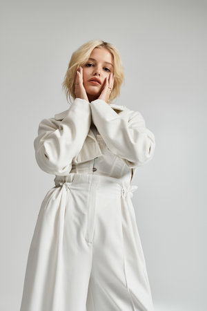 A stylish young blonde woman poses gracefully in a grey studio, highlighting winter fashion.の写真素材