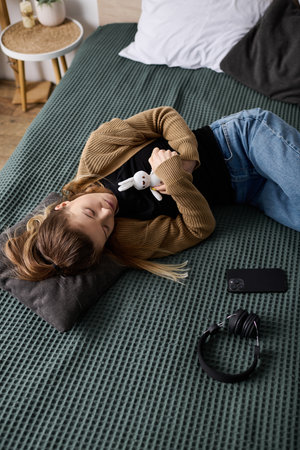 A young woman relaxes in her bed, holding a toy, surrounded by a cozy bedroom atmosphere.の写真素材