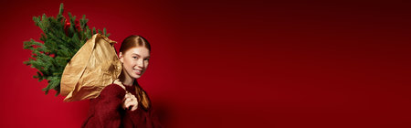 A young woman with red hair enjoys the festive season while posing in a cozy winter sweater, bannerの写真素材