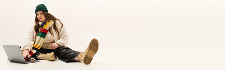 Young woman enjoys her cozy knitted sweater while working on a laptop.の写真素材