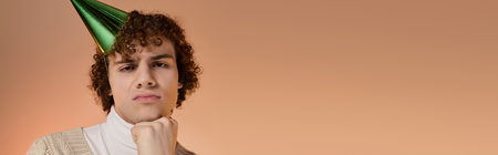 A bored teenage boy with curly hair poses thoughtfully in a party cap, bannerの写真素材