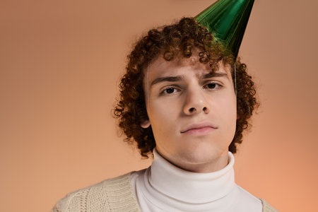 A curly-haired teen in a festive hat and knitted vest looking at cameraの写真素材