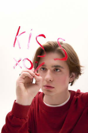 Young man in a red sweater writes kiss on a white surface, showcasing his creative spirit.の写真素材