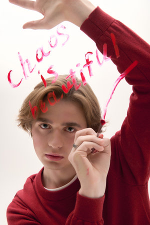 Young man shows unique style while writing on a plain background with vibrant colors.