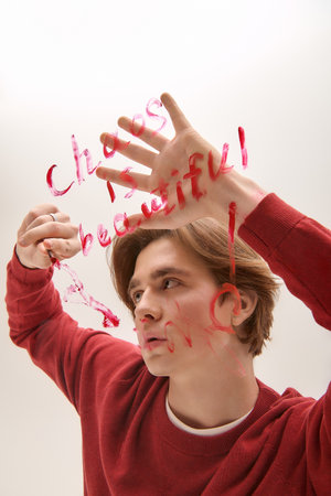 A young man in a red sweater writes creatively on a blank page.