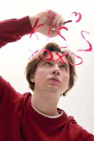 A young man in a fashionable outfit writes a loving message on a glass surface, expressing emotion.