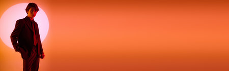 A young man stands in a fashionable outfit, exuding confidence with a vibrant sunset behind him.の写真素材