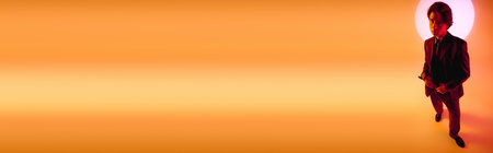 A stylish young man poses against a vibrant orange sunset, exuding confidence.