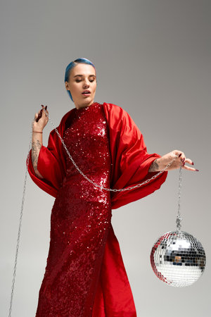 A beautiful young woman exudes festive charm in a glittering red outfit, holding a disco ball.の写真素材