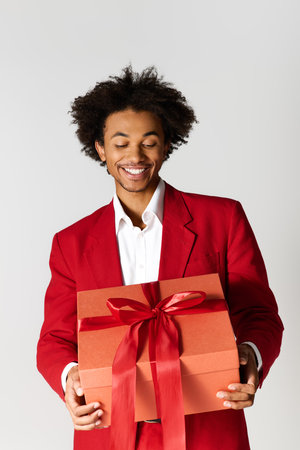 A young handsome man in an elegant red suit happily holds a beautifully wrapped gift, radiating joy.の写真素材