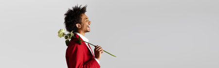 A young man dressed in stylish red attire smiles brightly while holding a rose, radiating happiness.の写真素材