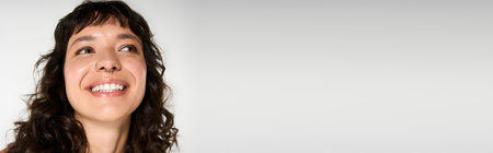 Young woman with curly hair smiles brightly, showcasing her stylish outfit in a bright environment.の写真素材