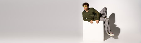 A young man with curly hair and sunglasses strikes a fashionable pose in a studio, bannerの写真素材