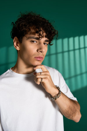 Curly-haired man poses thoughtfully, highlighting his modern fashion sense.の写真素材