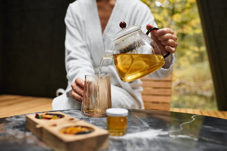 Young woman in a white bathrobe pours herbal tea at a modern spa, savoring her relaxing day.の写真素材