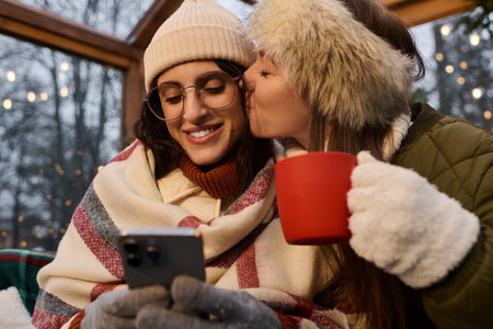 Two beautiful women enjoy a warm winter day together, sharing affection and laughter.の写真素材