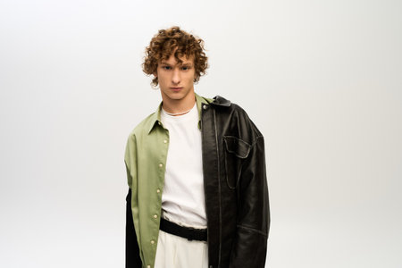 A handsome young man poses in trendy attire, exuding charisma in a simple studio backdrop.の写真素材