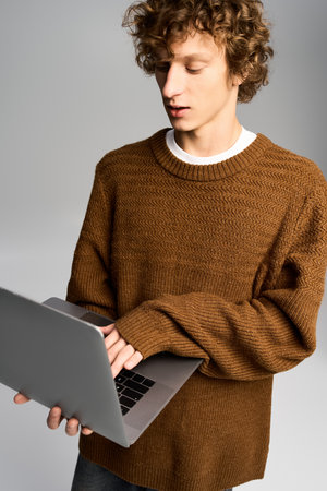 Handsome young man wearing a trendy sweater focuses on his laptop while seated in a stylish space.の写真素材