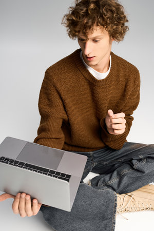 Handsome young man dressed in trendy attire interacts with a laptop, showcasing his style and focus.の写真素材