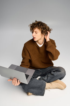 A stylish young man sits cross legged, focused on his laptop in a bright, minimalist studio space.の写真素材