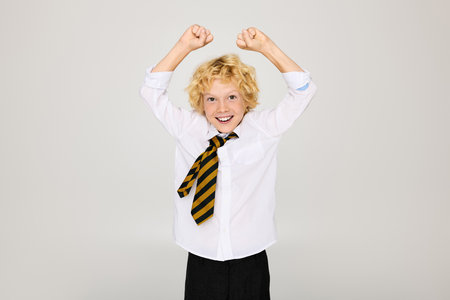 A happy blonde boy with wavy hair is celebrating in a studio while wearing a school uniform.の写真素材
