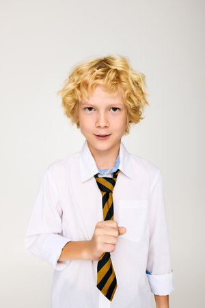 A young boy with wavy blonde hair stands confidently in a school uniformの写真素材