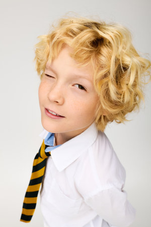 A cheerful blonde boy in a striped tie smiles and winks playfully in a studio.の写真素材