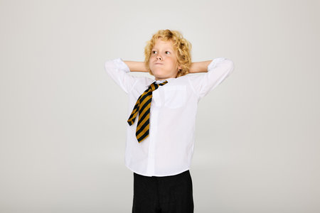 A blonde boy with wavy hair relaxes in his school uniform, puffing cheeks