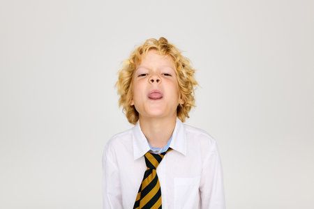 A cheerful blonde boy in a white shirt and striped tie playfully sticks out his tongue.