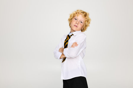 A young boy stands proudly in a school uniform with wavy blonde hair and a striped tie.の写真素材
