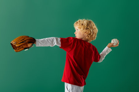 A young boy with wavy blonde hair throws a baseball while wearing casual red clothes in a studio.の写真素材