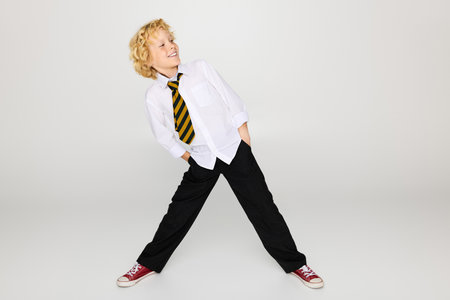Joyful blonde boy in a school uniform poses confidently with hands in pockets.の写真素材
