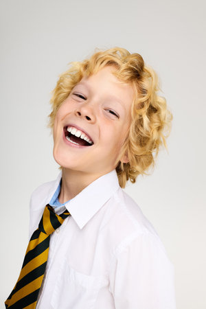 A cheerful blonde boy in a school uniform with a striped tie smiles brightly, radiating joy.の写真素材