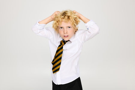 A blonde boy with wavy hair showcases his school uniform while posing in a studio.の写真素材