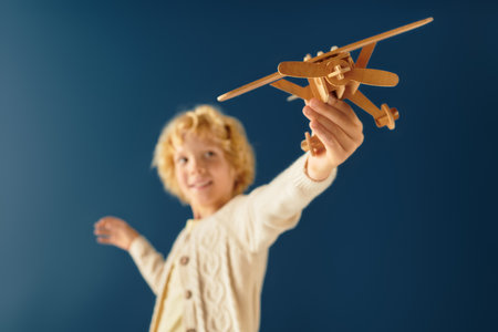 A young boy beams with happiness while holding a wooden airplane against a blue background.の写真素材